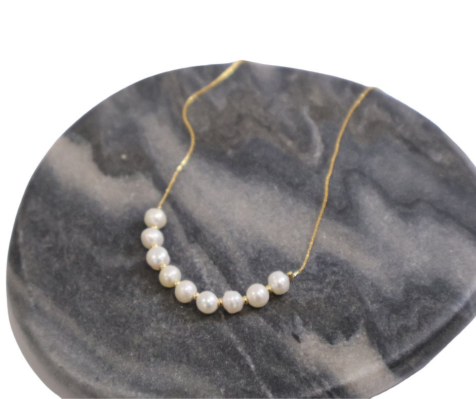 Pearl necklace on a gold chain displayed on a grey marble surface - bridal jewellery