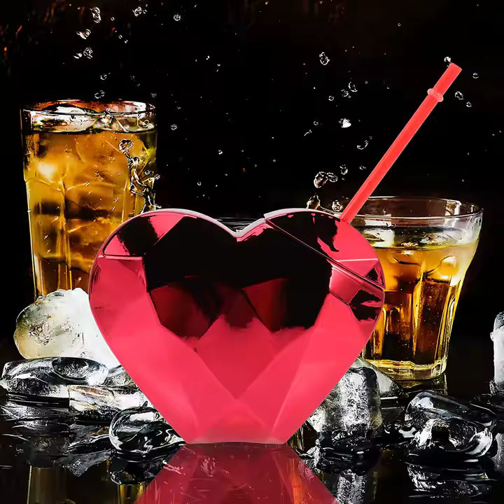 Heart-shaped drink tumbler with ice cubes and glasses of iced liquid on a dark background