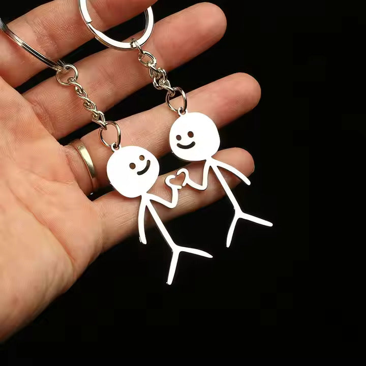 Two white stick figure keychains held by a hand against a black background