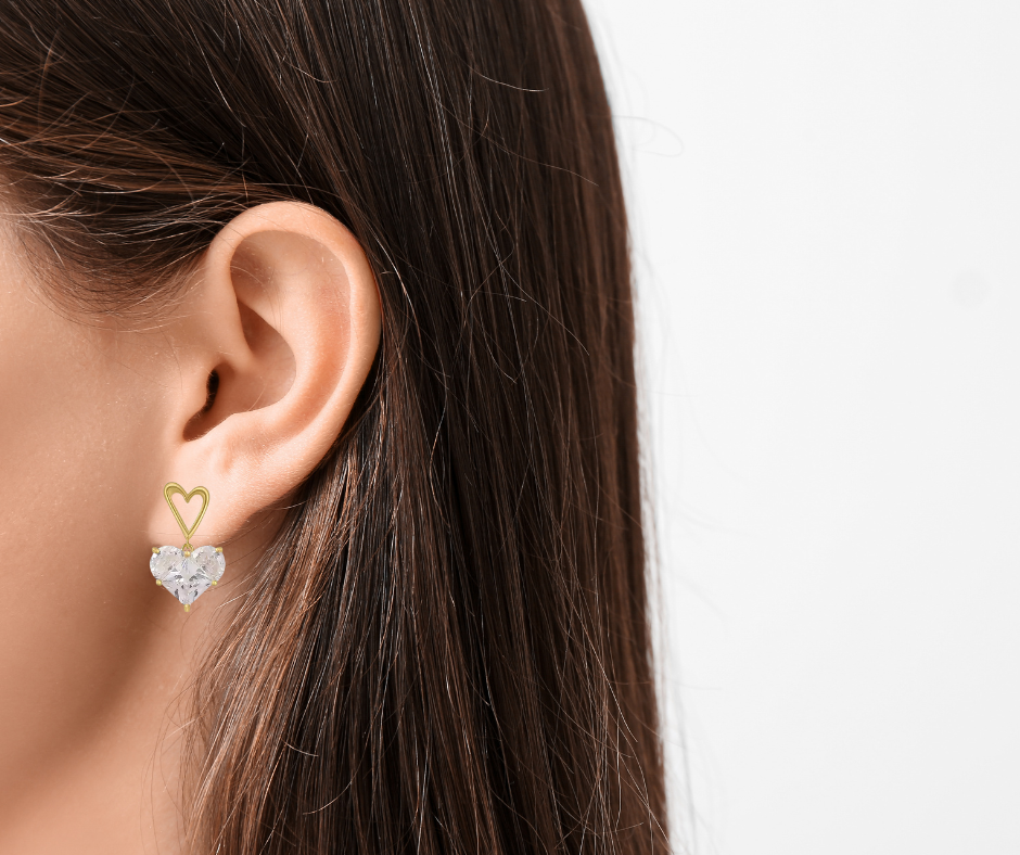 Heart-shaped earrings worn by a person with long hair on a neutral background