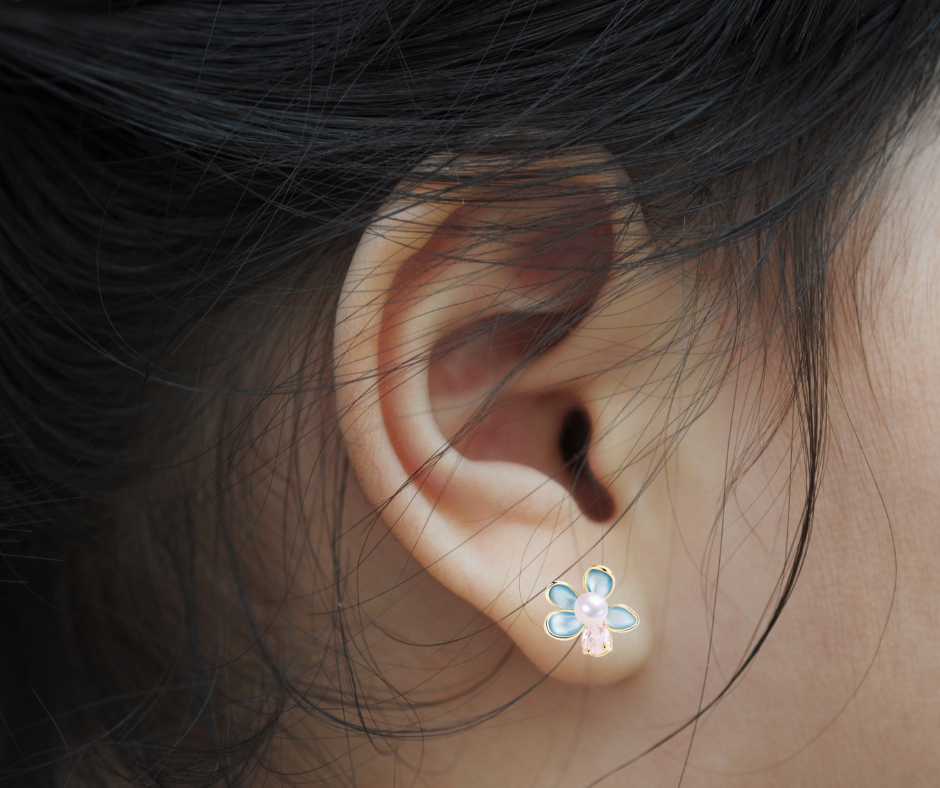 Close-up of an ear wearing a floral pearl earring with dark hair.