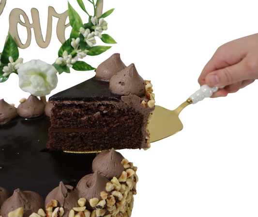 Chocolate cake with a slice being lifted by a cake server, decorative flowers and 'Love' sign in the background.