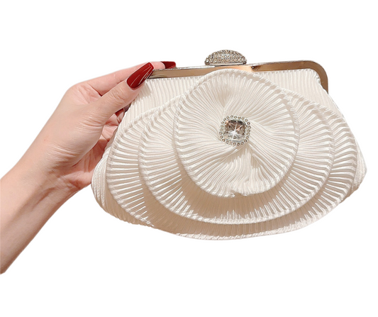 Hand holding a white pleated clutch bag with floral design and gemstone embellishments on a white background