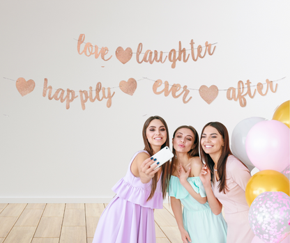 Three women taking a selfie with balloons and a "Love, Laughter, Happily Ever After" decorative banner in the background.