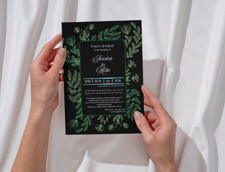 Hand holding a wedding invitation with green leaf design against a white curtain background