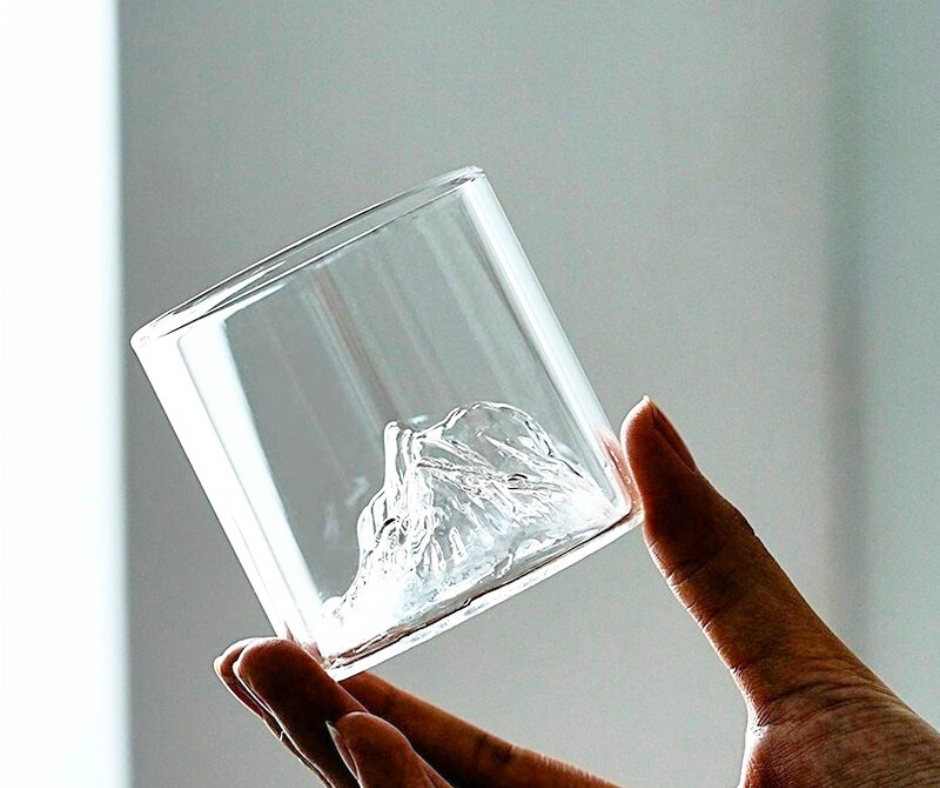 Hand holding a clear glass with a mountain design against a plain background