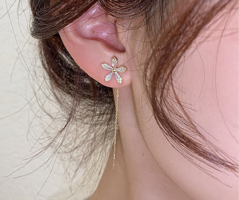 Close-up of an ear wearing a floral earring with a delicate chain.