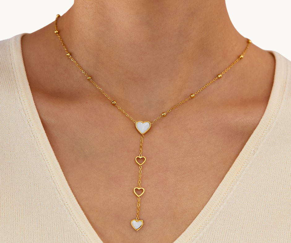 Gold pearl shell necklace with heart pendants on a person wearing a beige top