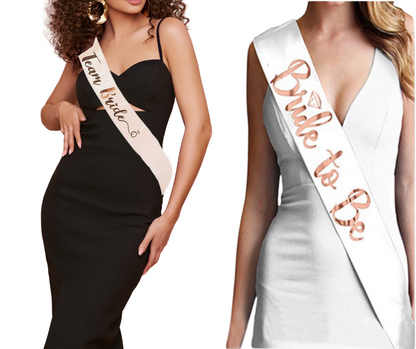 Two women wearing 'Bride to Be' and 'Team Bride' sashes on a plain background