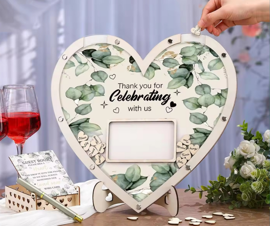 Heart-shaped wooden guest frame with eucalyptus design, placed on a table with wine glasses and flowers.