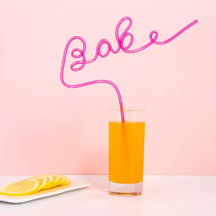Glass of orange juice with a pink 'Babe' straw shaped on a pink background