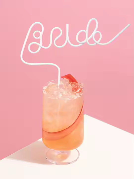 Cocktail with ice and a bride straw on a pink background 