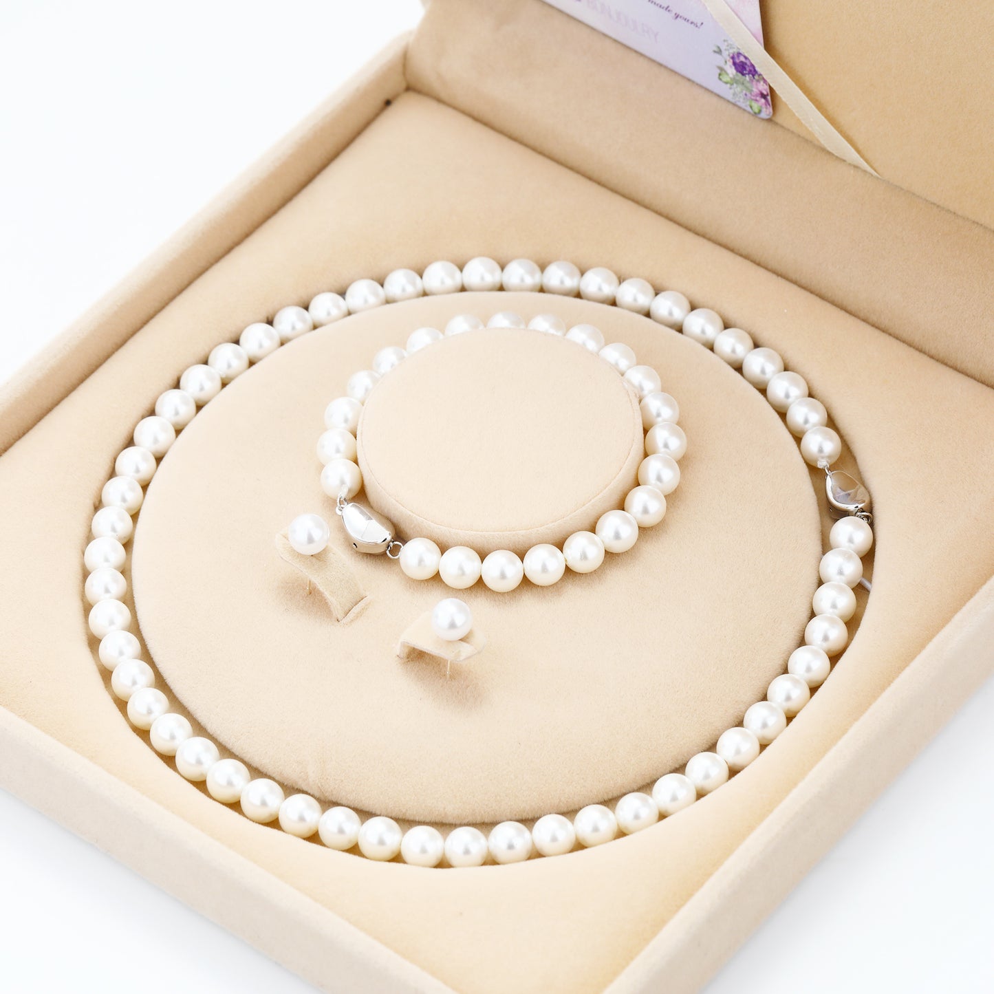 Pearl necklace and bracelet set in a beige jewelry box on a white background