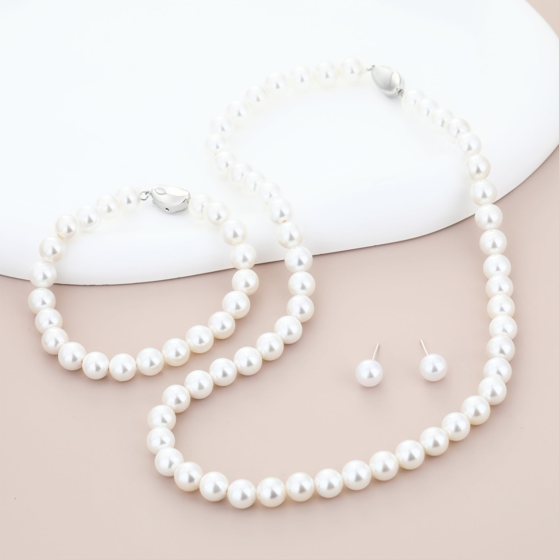 Pearl necklace, bracelet and earrings set on a beige surface with a white background
