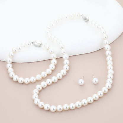 Pearl necklace, bracelet and earrings set on a beige surface with a white background