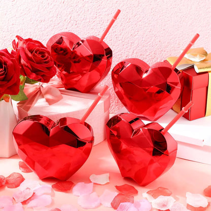 Red heart-shaped tumblers with straws on a romantic setting with roses and gift boxes.