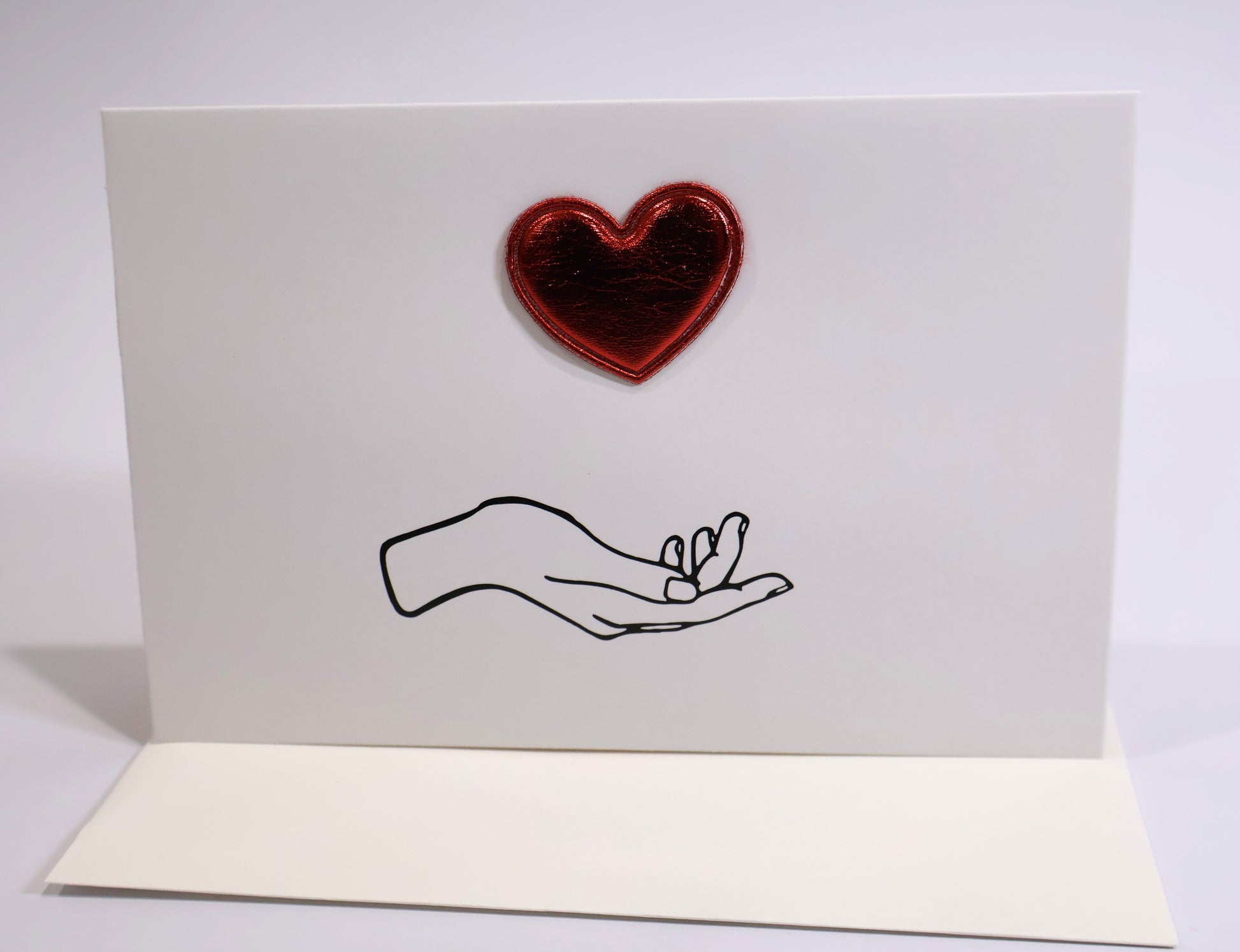 Card with a red heart and black line drawing of a hand holding a heart on a white background