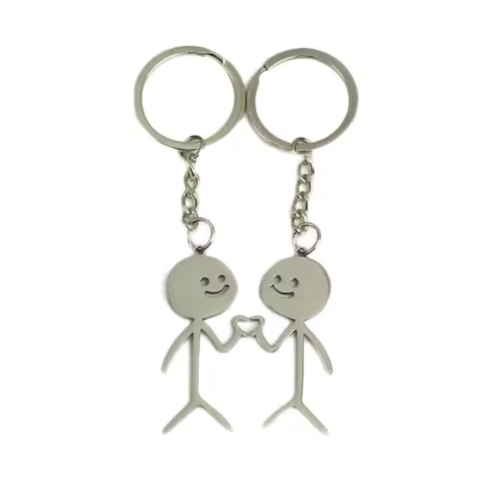 Two silver keychains shaped like stick figures holding hands on a white background