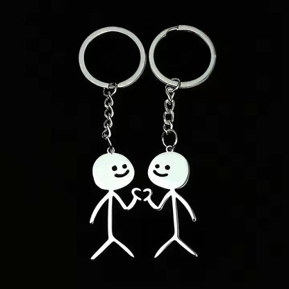 Two silver keychains shaped like stick figures doing heart hands on a black background