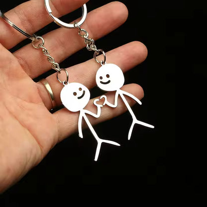 Two white stick figure keychains held by a hand against a black background