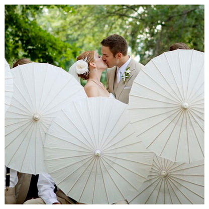 Wedding couple kissing under white parasols with a forest background