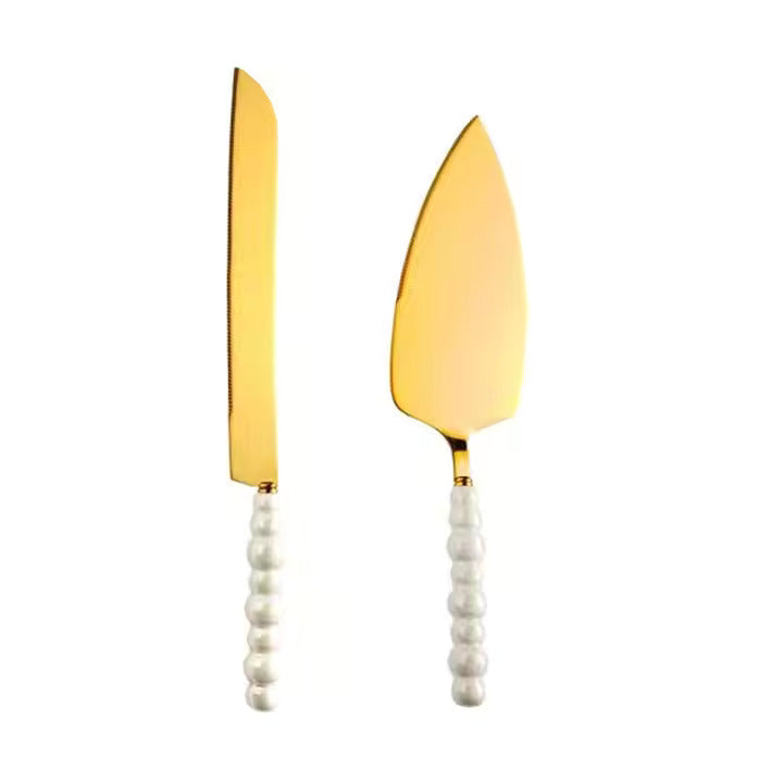 Gold cake knife and server set with white pearl like handles on a white background
