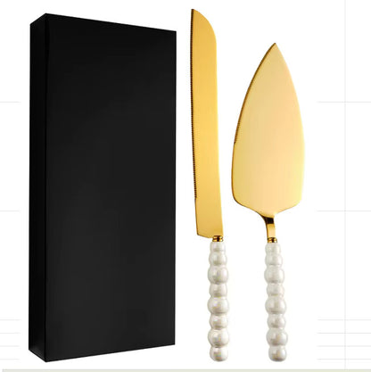 Gold cake knife and server with white pearl like handles next to a black box on a white background