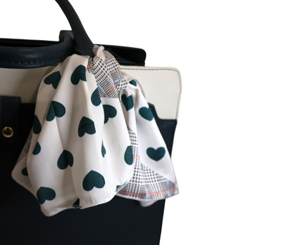 White bag with a green heart patterned scarf draped over it on a white background