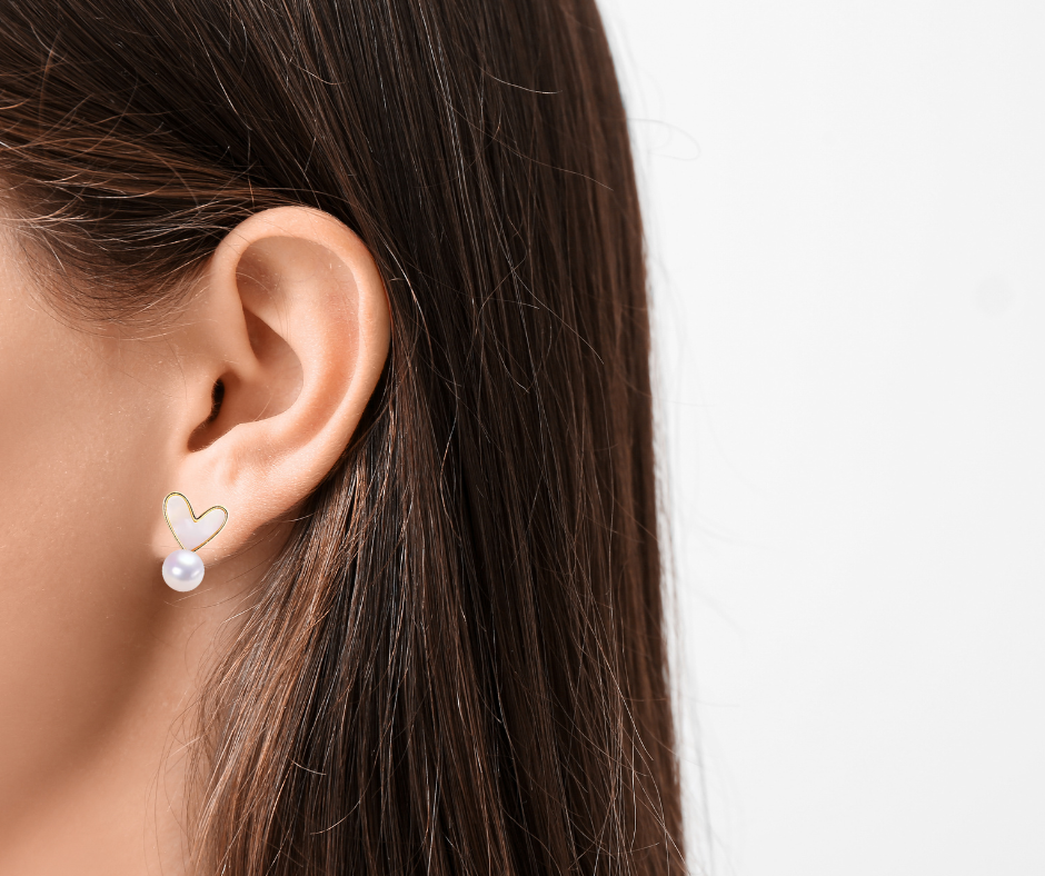 Close-up of an ear wearing a heart-shaped pearl earring with a blurred background