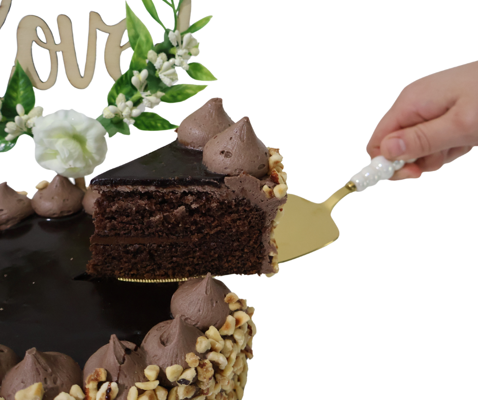 Chocolate cake with a slice being lifted by a cake server, decorative flowers and 'Love' sign in the background.