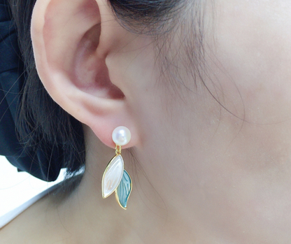 Close-up of an ear wearing a pearl earring with leaf-shaped gold and green charms.