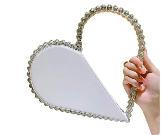 Hand holding a white heart-shaped handbag with rhinestone handle on a white background