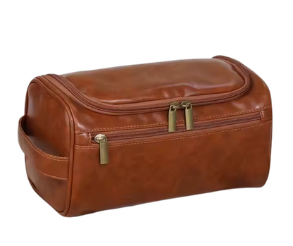 Brown leather toiletry bag with gold zippers on a white background