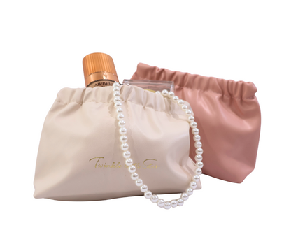 Perfume bottle, pearl necklace, and a white and pink makeup clutch on a white background